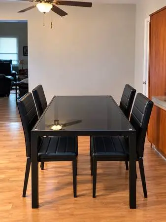 Black dining room table with glass top and four matching chairs.